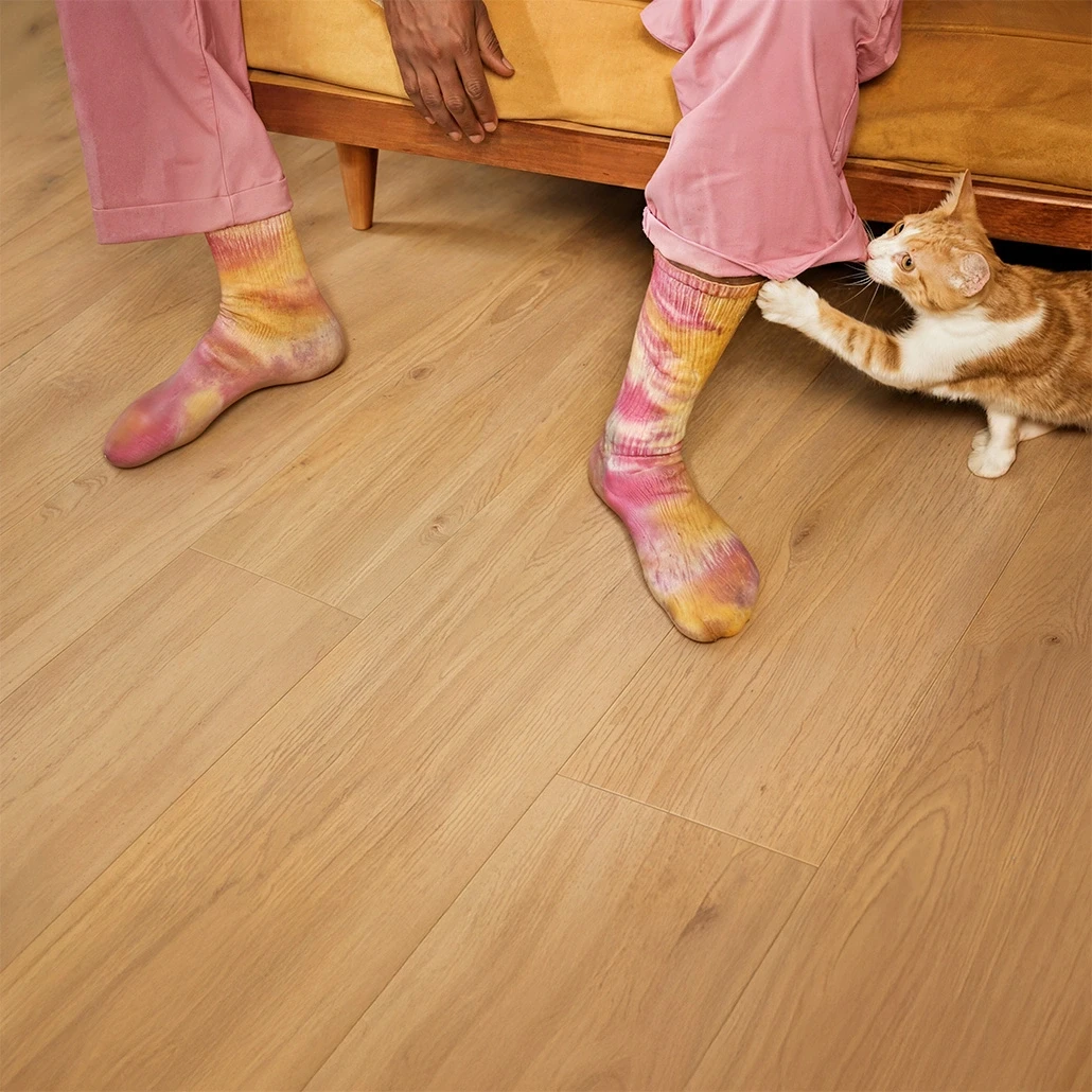 Eine Katze zieht eine Person an den Socken, während sie auf einem mit Kiwi-Now-Bodenpaneelen des Modells 40KN792 ausgelegten Boden sitzt.